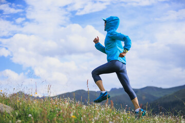 Fitness woman runner running at flowering grassland mountain top