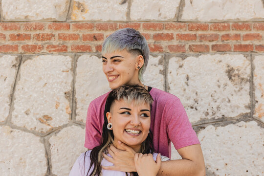Lesbian couple laughing and embracing against a brick wall