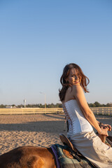 Fototapeta premium Young and beautiful Kazakh woman is on a brown horse in the countryside. Riding against blue sky.