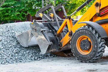 A yellow tractor with front hydraulic buckets rakes gravel at a construction site.