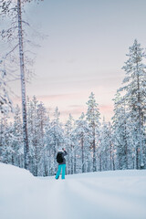Woman Influencer in a Snow Suit Taking Phone Pictures in the Snow Covered Forest