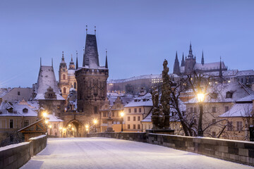 Naklejka premium View of Lesser town tower of Charles Bridge with Prague Castle in the background in Prague during in the early morning in winter under the snow. Czech Republic.