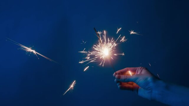 Detail view of hand holding glowing spark of firework burning for celebration on blue wallpaper