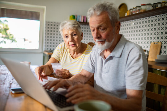 Elderly couple managing bills and finances on laptop in kitchen