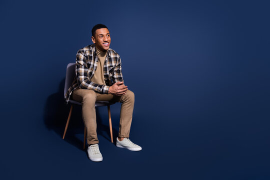 Full length photo of handsome good mood guy wear checkered shirt sitting stool looking emtpy space isolated blue color background - Powered by Adobe