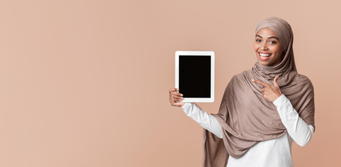 Smiling Afro Muslim Girl Pointing At Digital Tablet With Black Screen, Posing Over Yellow Background, Free space