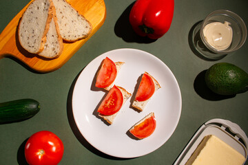 Sliced toast with butter and tomatoes on the white plate. Flat lay of the breakfast on dark green background. Traditional breakfast concept. Top view