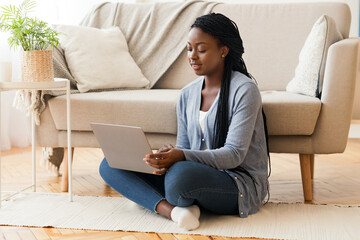 Young African American Girl Sitting On Floor With Laptop, Working From Home.