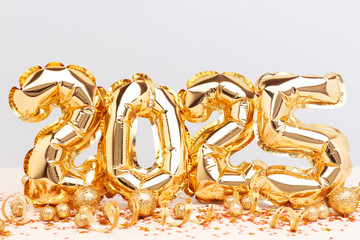2025 New Year celebration concept. Golden inflatable balloons with confetti in front of blue and beige background.