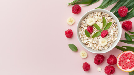 A colorful bowl of oatmeal topped with bananas, raspberries, and mint leaves, surrounded by fresh fruit and green leaves on a pink background.