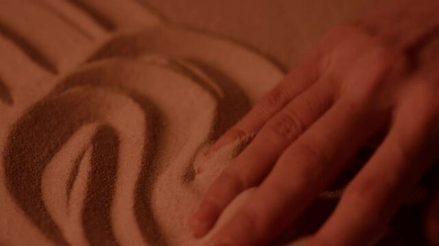 Detail view of female hand erasing lines in sand with palm making smooth movements from side to side