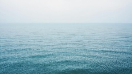 Obraz premium Tranquil blue ocean water with a soft, misty sky above.