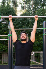 Fototapeta premium Front view of sporty man doing pull ups on horizontal bar outdoors. Young man street workout exercising at the morning time