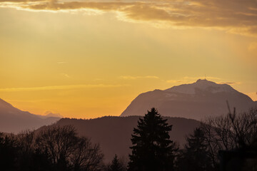 Breathtaking sunset over silhouette of forest and majestic mountain peak Dobratsch in Carinthia, Austria, Europe. Sky is ablaze with vibrant hues of orange and red. Rosental in summer, Austrian Alps