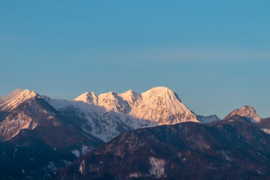 First sunrise sunlight on majestic snow-capped mountain summit Mittagskogel in Karawanks seen from Rosental, Carinthia, Austria. Alpine winter wonderland landscape at night in serene Austrian Alps - Powered by Adobe