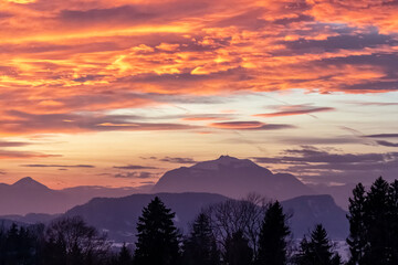 Breathtaking sunset over silhouette of snow-capped majestic mountain peak Dobratsch in Carinthia, Austria, Europe. Sky is ablaze with vibrant hues of orange, pink. Rosental in winter, Austrian Alps