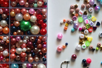 Colorful beads, letter beads, threads and other jewelry making supplies on white background. Making friendship bracelets concept. Flat lay.