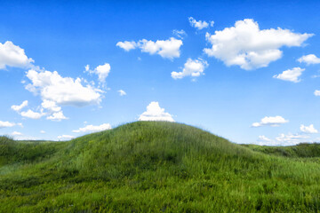 a green meadow and hills under an open blue sky with clouds.