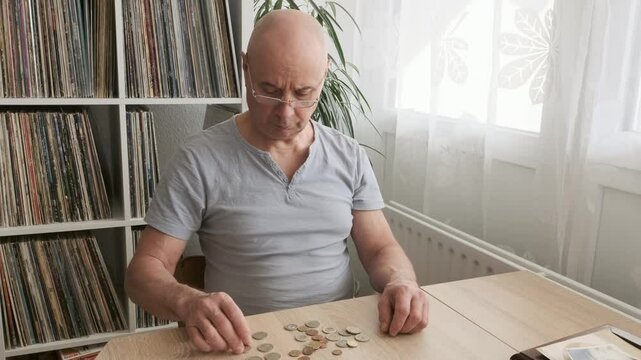 poor pensioner, Senior man with reading glasses lays out euro cent coins on wooden table, counts meager cash money on table, Struggle for Survival, harsh reality of life in poverty