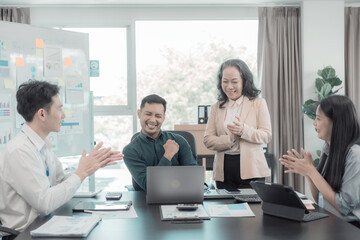 A diverse group of business professionals gather at a conference table in an office to celebrate a business victory, a good sales result, and achieving a financial goal.