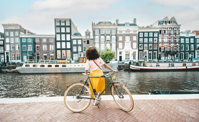 Happy female tourist visiting Amsterdam city, Netherlands - Delightful woman riding bicycle in...
