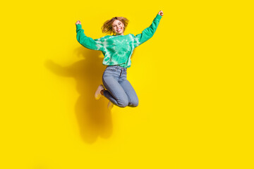 Obraz premium Full length photo of lucky positive woman wear green sweatshirt jumping high rising fists empty space isolated yellow color background