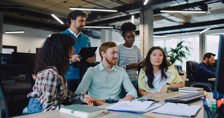 Multi-ethnic group of people together looking for solution to issue. Making important decision. Man in middle pointing at screen while his friends trying to explain their point of view. Difficulties.
