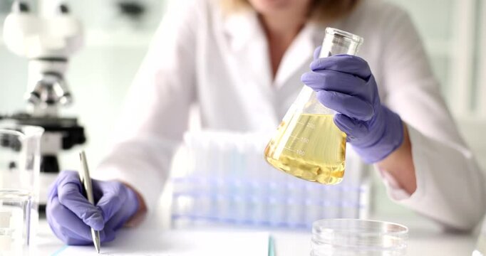 Scientist conducts laboratory testing of transparent yellow liquid in flask. Control of petroleum products in lab
