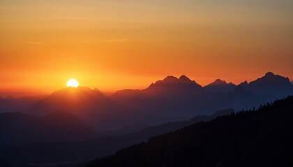 Obraz premium The sun sets behind a distant mountain range, casting warm orange and red hues over the silhouetted peaks and valleys.