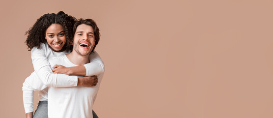 Piggyback ride. Affectionate guy carrying his black girlfriend on back, interracial couple bonding together over yellow background with free space