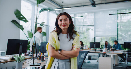 Confident Asian woman crossing hands while looking at camera in modern office. Happy about works...
