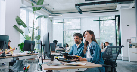 Camera view of beautiful woman sitting next to her coworker at desk in office. Specialists...