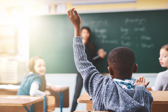 Little boy, hands raised and classroom with question for teacher, answer or learning at elementary school. Back view, kid or young child with answer for interaction, engagement or attention in lesson