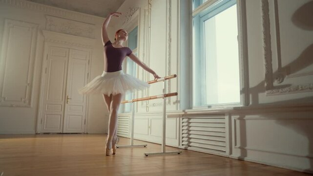 Professional young ballerina in rehearsal room, graceful figure in tutu. Classic music and ballet dance, woman practicing dancing on pointe shoes on parquet, slow motion shot, beauty and art concept