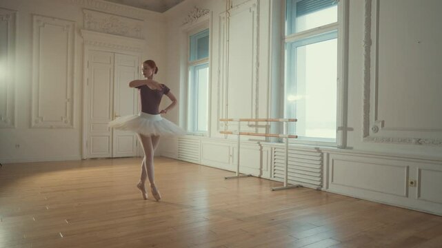 Slender graceful ballerina in tutu dancing in rehearsal room, slow motion. Attractive female ballet dancer exercising in dance hall, standing on parquet with pointe shoes, classical dance performance