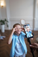 Naklejka premium Boy takes photo of himself on his mobile phone. He smiles and makes faces. Fun and playfulness concept. Selective focus. Vertical image.