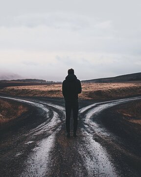 A person standing at a crossroads, torn between two paths, with an expression of deep uncertainty and anxiety, symbolizing a difficult decision and inner struggle.