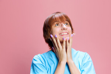 Portrait of young girl with short hair, looking upwards with dreamy and happy expression against pink studio background. Concept of human emotion, youth, lifestyle, fashion