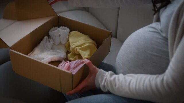 Woman pregnant unrecognizable female girl mother unpacking parcel box delivery service post unpack child cloth kid tiny little shoes put on big belly tummy anticipation child medicine shopping concept