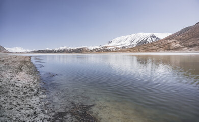High-mountain lake Khargush with snow and ice on the surface of the water against the backdrop of mountain rocky peaks with snow in the Tien Shan mountains in Pamir in Tajikistan, landscape