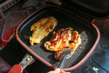 Close up of two chicken thighs being fried in a black frying pan with a red border. The chicken has a nice golden brown color and looks delicious. The photo is taken from a slightly overhead angle.