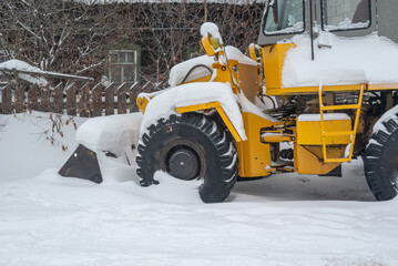 A bulldozer for clearing roads of snow during a snowfall. A bulldozer with large wheels for road construction works stands in a snowdrift in winter. Road equipment.