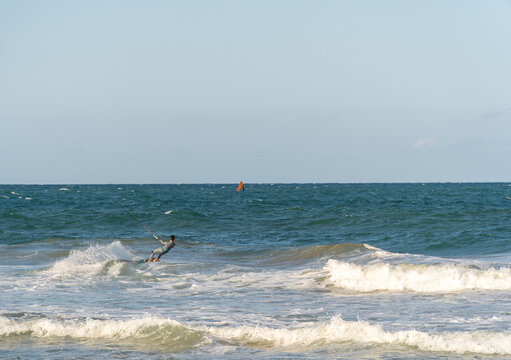 A young man kitesurfing at sunset in the sea.