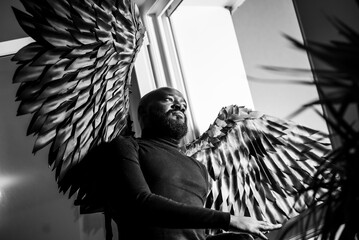Elegant man with large wings contemplating by window in black and white
