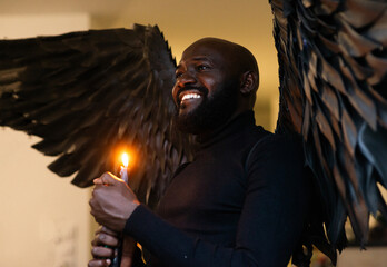 Man with black wings holding candle and smiling in dim light
