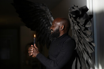 Man with black wings holding a candle in dark atmosphere