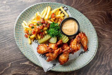 plate of crispy fried chicken wings, golden French fries, pickles, and a side of salsa, accompanied...