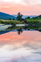 Amazing view at scenic landscape on a beautiful lake and colorful sunset with reflection on water surface among green reeds and glow on a background, spring season landscape