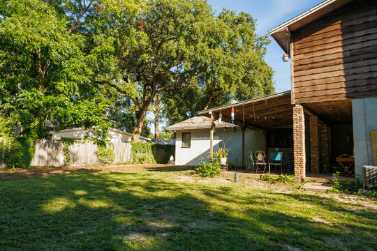 Late afternoon view of a large house with an expansive covered patio from the back yard with green grass and dappled light, Florida, USA