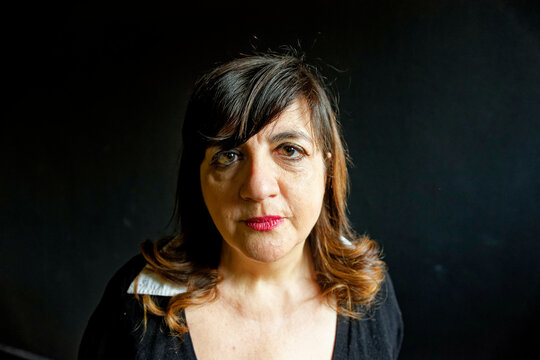 Fish-eye view of a woman with shoulder-length hair standing against a black background, looking slightly to her right with a serious expression.